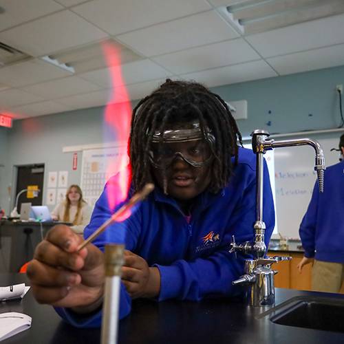 High school boy holding a vial in a Bunsen burner during a science class experiment